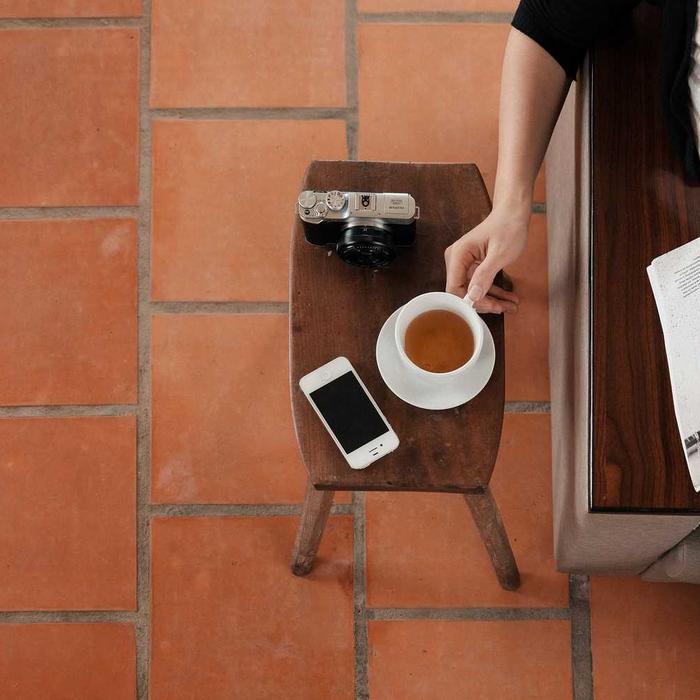 A cup of coffee, a phone and a camera on a small table over terracotta tiles
