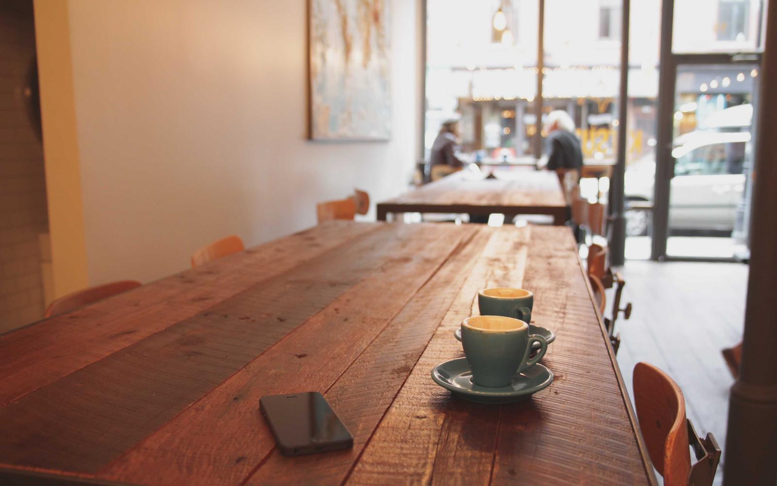 Sunlit café interior with a long wooden table, coffee cups and big windows