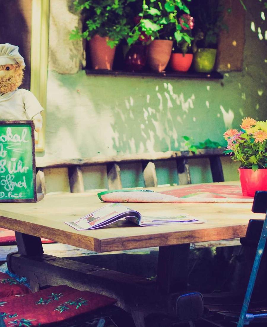 Our garden patio: a wooden table in dappled light, with plants and a chalkboard