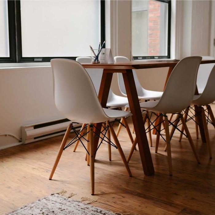 Light wooden table and white chairs by a large window