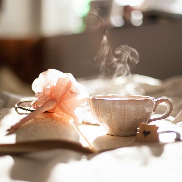 Steam rising from a cup of tea beside a pink flower