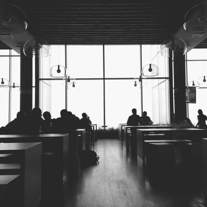 Silhouettes of guests against tall café windows