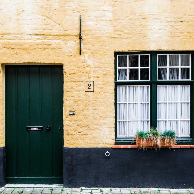 A green door and a window with white curtains on a yellow-painted wall