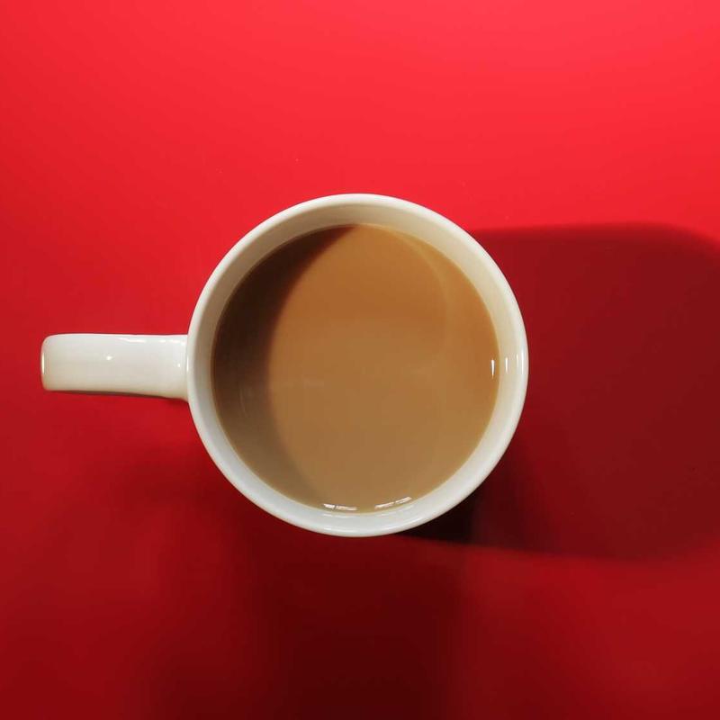 A cup of milky tea on a red table, seen from above