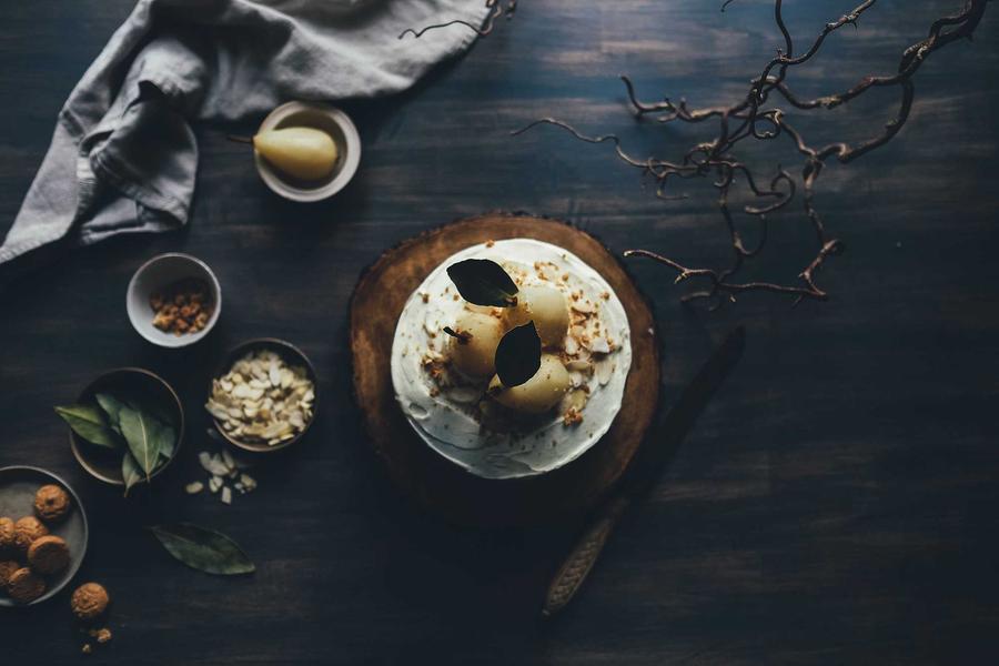 A dessert of poached pears and cream on a dark table with small bowls of nuts