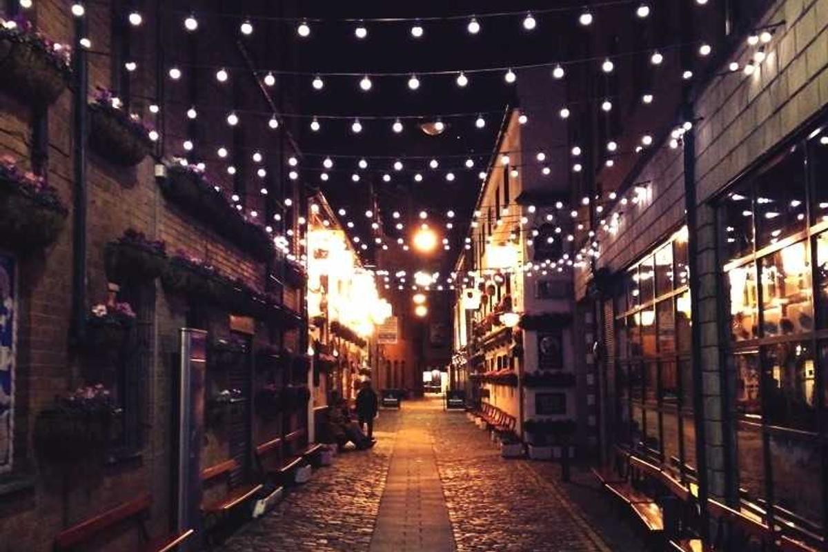Strings of warm festoon lights glowing over a lane at night