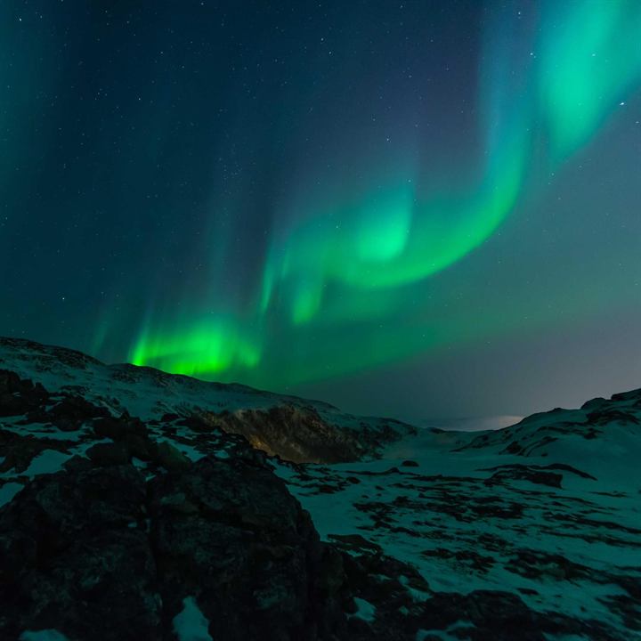 Green aurora curling over dark snowy hills