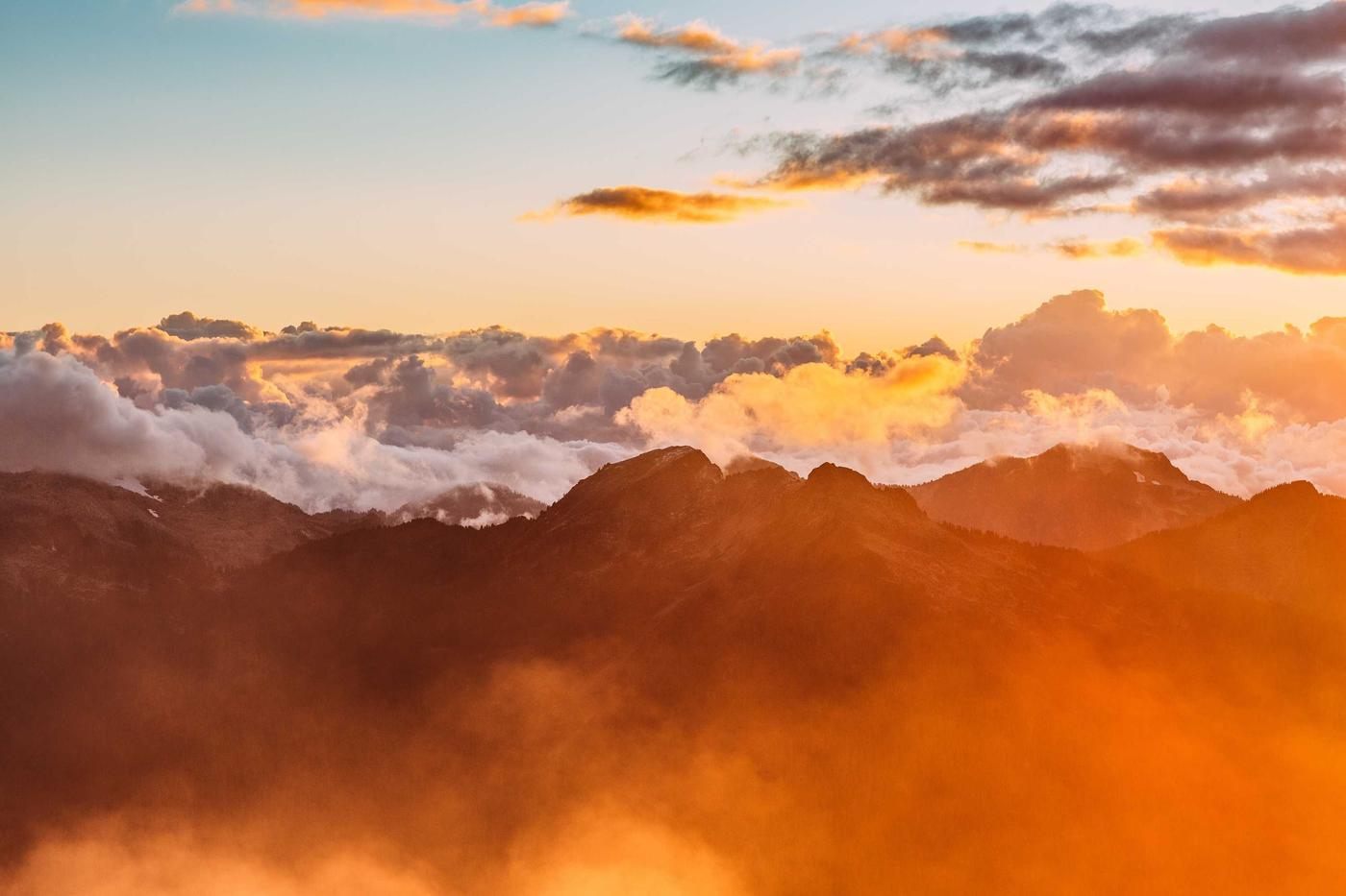 Sunrise over a sea of cloud, orange light on mountain ridges below a banded sky