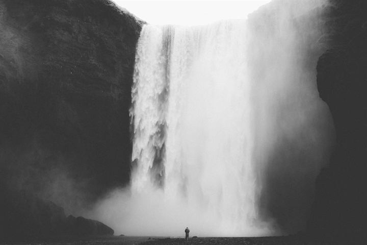 Black and white photograph of a tall waterfall with a tiny figure at its foot